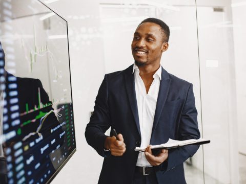 African man in a black suit. Big TV screen. Guy shows presentation.