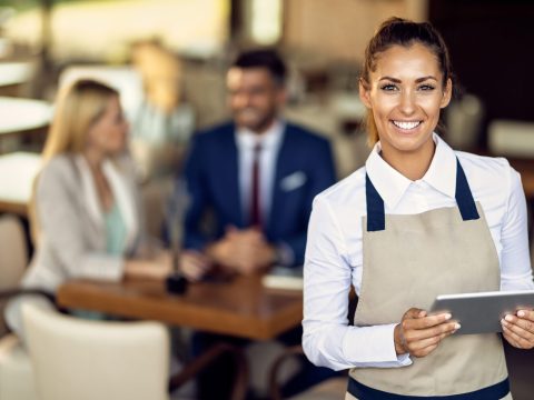 Happy waitress working on digital tablet in a cafe and looking at camera.